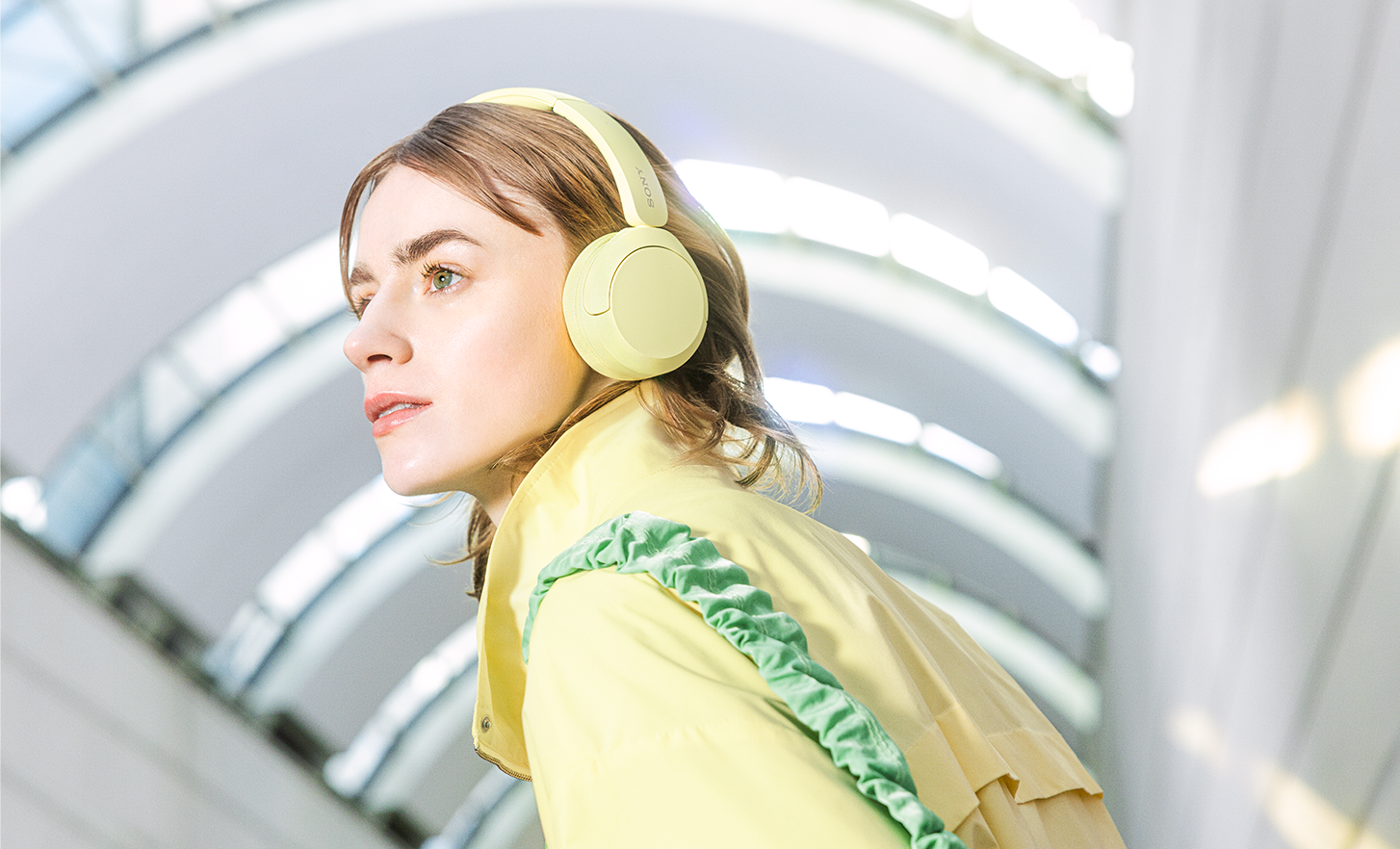 Una persona con unos auriculares WH-CH520 en amarillo de Sony vestida con una chaqueta a la moda que combina.