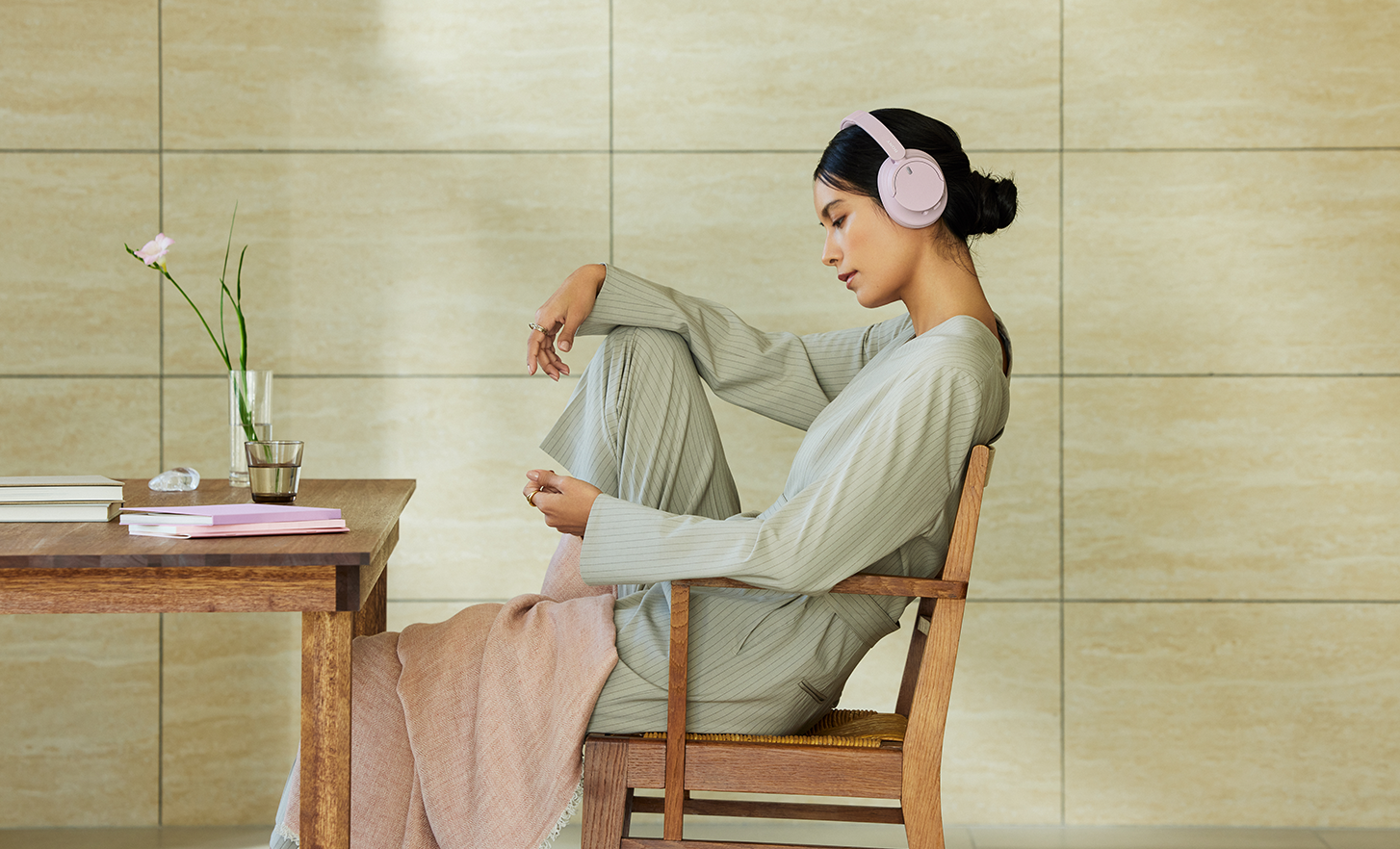 Una persona con unos auriculares WH-CH720N en rosa de Sony, se relaja en un espacio minimalista.