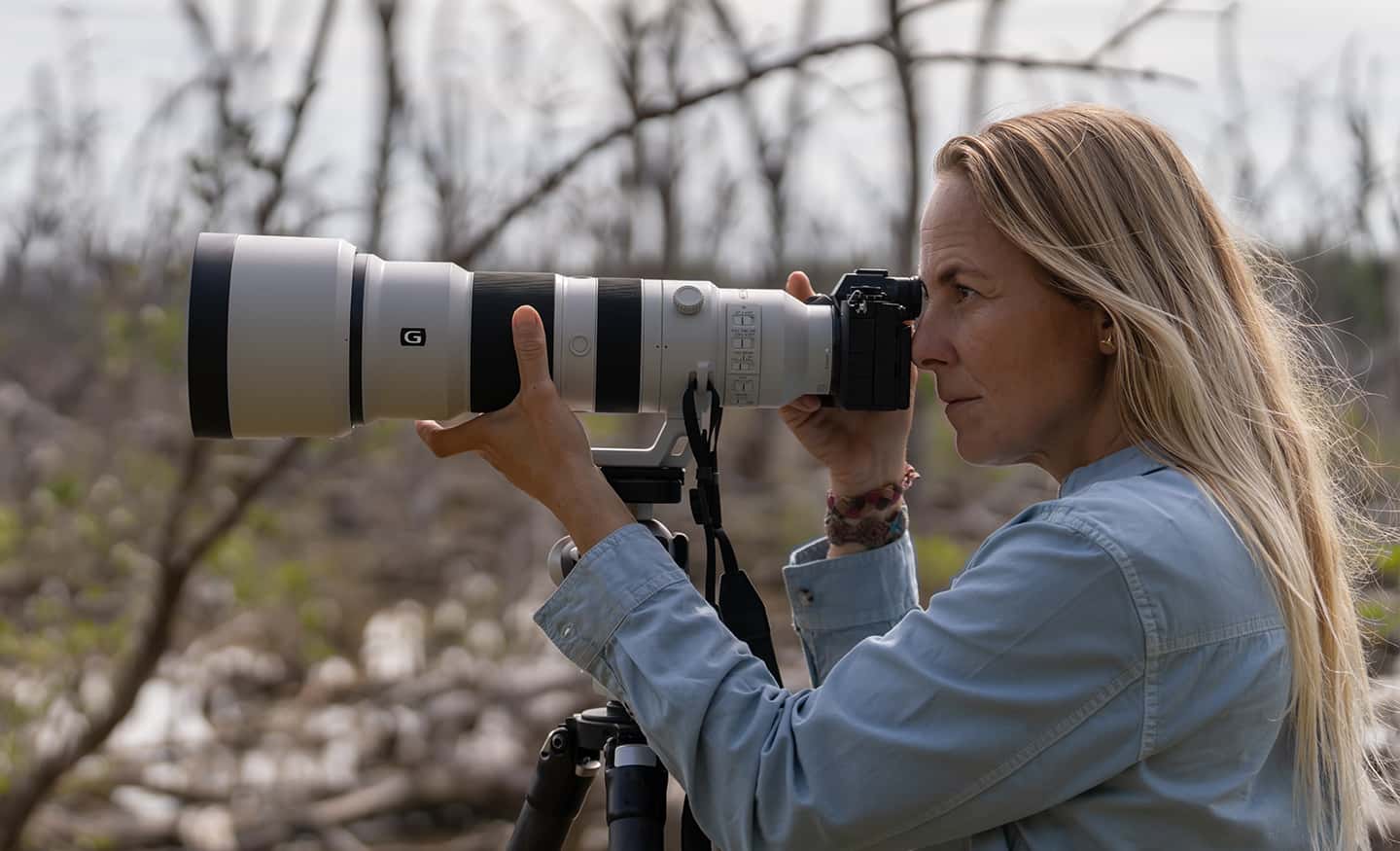 Imagen de uso que muestra a una mujer mirando a través del visor de una cámara montada en un trípode a través de la montura del trípode de la lente