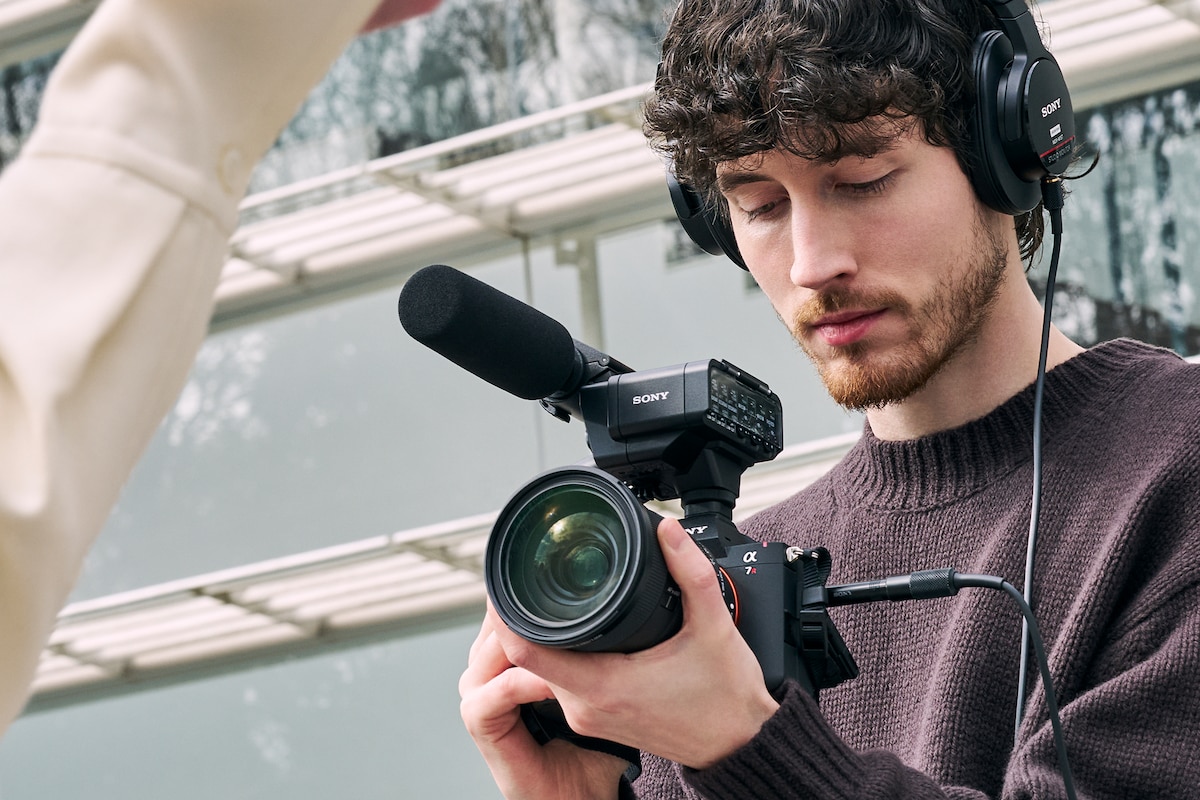 Imagen de uso que muestra a un hombre con auriculares conectados a la α7R VI con el adaptador XLR XLR-A4 y el micrófono direccional ECM-778 acoplado, que capturan audio y video.