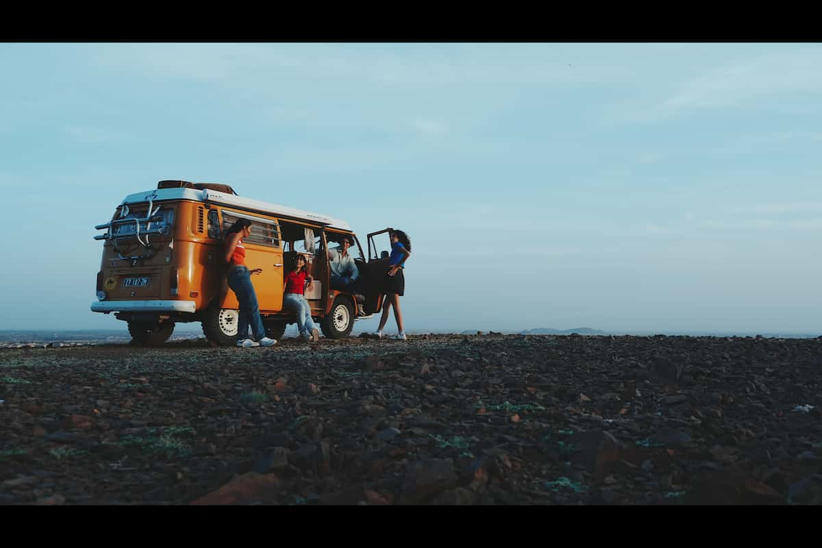 Imagen de ejemplo de cuatro hombres y mujeres charlando alrededor de una autocaravana naranja